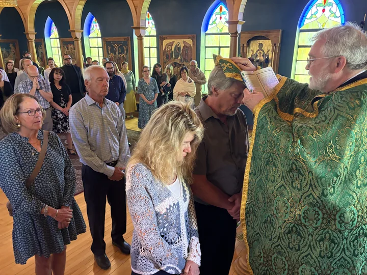 A priest praying over a bowed head as others gather alongside