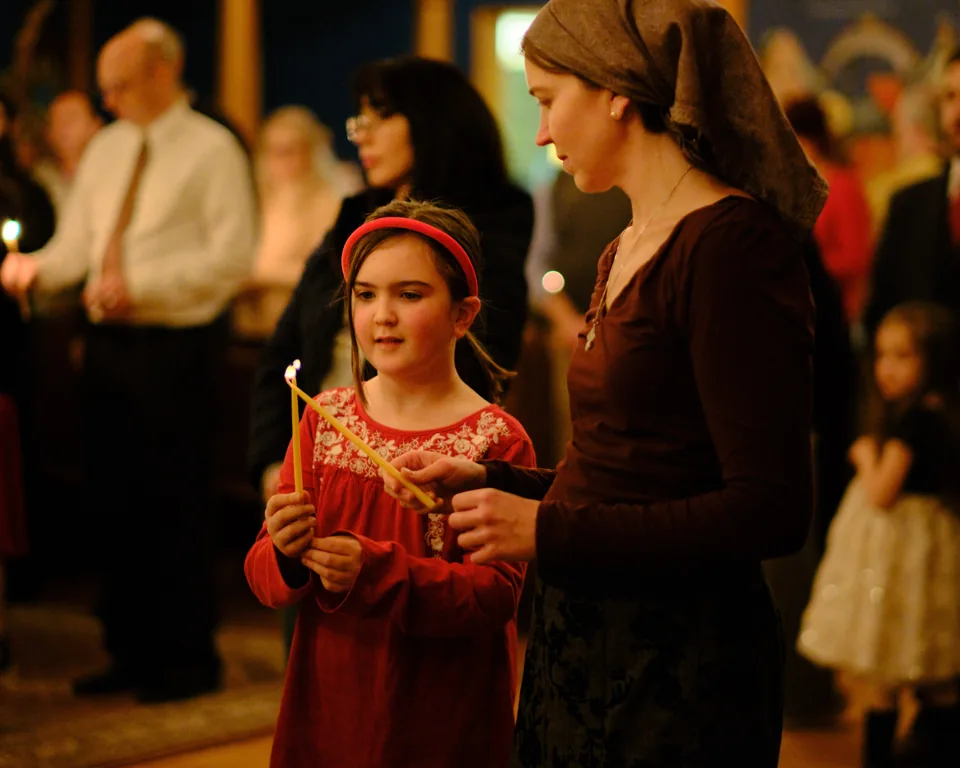A child and an adult holding lit candles among parishioners during worship